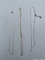 Three necklaces displayed flat on a white surface: two gold chains and one silver chain with pendants.