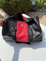 Photo of black and red GUESS duffle bag showing front with logo and handles.