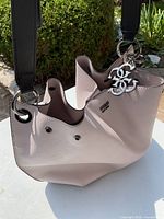 Soft greyish pink Guess bucket style purse showing front and side with black shoulder strap and silver hardware
