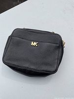Front view of small black purse showing pebbled leather and gold MK logo