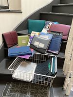 Various colored file folders, binders, and document holders arranged on stairs around a white wire basket