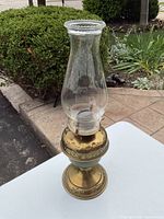 Vintage oil burning lamp pictured outdoors, showing full lamp and surroundings