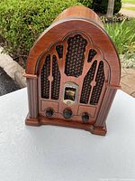 Front view of vintage wooden cathedral style radio showing carved wood design, fabric speaker grille, tuning dial and three black control knobs.
