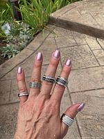 Hand wearing multiple silver-tone rings with clear rhinestones and textured details showing various styles in outdoor natural light.