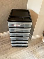 Front view of the black and clear plastic 6-drawer storage unit on wheels, showing the top surface with compartments and partially visible drawer contents.