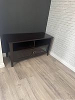 Dark wood TV stand shown placed between dark and white brick walls with wooden floor.