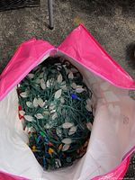 Top-down view into pink and white storage bag showing tangled string of white faceted C7 style Christmas lights with dark green wiring.