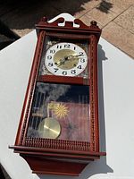 Full front view of wooden wall clock showing clock face and pendulum behind glass door.