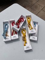 Six ZARA leather key chains in blue, red, and yellow, boxed individually on a tiled surface.