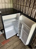 Black Danby Premier bar fridge with open door showing interior shelving, wire rack and door compartments for bottles and storage.