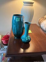 Two Blue Mountain Pottery vases on a wooden surface, the smaller one measuring 8.5 inches and the larger one 10 inches tall, both with blue-green glaze.