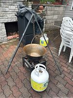Hungarian bogracs pot hanging on black metal tripod with propane burner and propane tank visible in background on brick patio