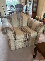 Front view of a damask and striped fabric upholstered armchair with rolled arms, rounded backrest, and patterned fabric upholstery