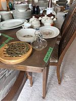Table with stacks of dishes, covered soup bowls with lids in floral and brown stripe patterns, a glass cruet, teacup and saucer, and serving platters shown