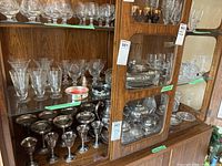 Wide view of hutch shelf showing assorted crystal and glassware items including glasses, vases, metal and glass serving pieces.