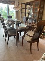 Dining table with 6 chairs, 2 with arms and 4 without, arranged around the table with dishes on top in a dining room setting.