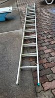 Full length view of the 12 foot aluminum extension ladder outdoors on a sidewalk and brick surface.