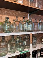 Shelves filled with multiple clear glass gallon jugs with different styles of lids and stoppers, stored in a basement cold room