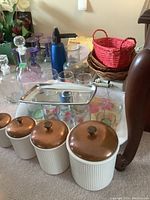Photo showing four vintage ribbed ceramic cannisters with coppertone lids, glass decanters, Precisa kitchen scale, wicker baskets, cocktail spritzer, and plastic wine glasses.