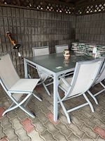 Full view of patio table with six chairs around it, showing mesh chair backs and floral cushions stacked on table.