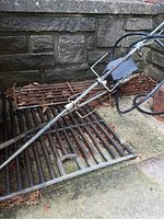 Photo of one rotisserie spit resting on two metal cooking racks against a stone background. Shows overall appearance and condition.