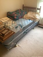 Single bed with wooden spindle headboard next to window, includes mattress, box spring, and bedding with sheets and comforters.