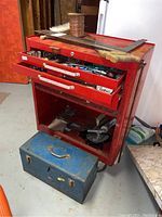 Front and side view of red metal tool chest with two drawers open, pull-down door open, and blue metal toolbox on floor.