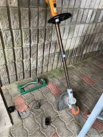 Full view of Black & Decker 20V trimmer, battery, charger, and green sprinkler on ground with brick wall background