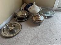 Photo of all items in the lot: tureen, silverplate trays, casserole holders, and divided serving dish on carpet.