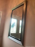 Rectangular wall mirror with brushed chrome and black edge wood frame, beveled glass edge, showing reflection of front door with stained glass panes.