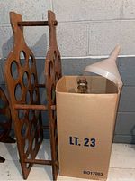 Wooden wine rack beside cardboard box labeled LT. 23, with white plastic funnel.