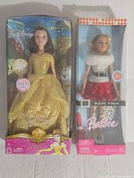 Both dolls in their original boxes, showing packaging and dolls inside. Belle's box has a visible dent and damage.