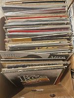 Top view of box packed with multiple vinyl records stacked vertically, shows album cover edges and some titles visible.