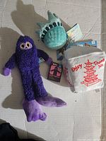 Lot of three new Bark brand dog toys with tags visible: purple Buddy Bigfoot, green Statue of Liberty, and white takeout box plush toys.