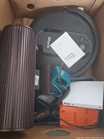 First image showing Shark robot vacuum, large cylindrical component, white and orange electronic devices, and charger cables in a box