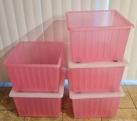 Five pink IKEA rolling storage totes stacked, three with white lids and two without lids, showing overall condition and shape.