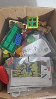 Box containing assorted Lego pieces including bricks, baseplates, windows, and instruction sheets seen from above.