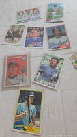 Photo showing a selection of vintage baseball cards arranged on a white surface featuring players in mid-action or portrait poses.