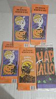 Four vintage-style Halloween door decorations in original packaging, featuring ghosts, jack-o'-lanterns, and bats on orange and black backgrounds with 'Happy Halloween' text.