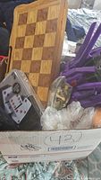 Box filled with wooden chessboard, various toys and game pieces, taken from a top angle.