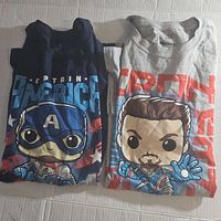 Pair of folded Marvel Avengers T-shirts, one navy blue Captain America, one gray Iron Man, both display Funko Pop styled graphics