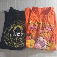 Two folded Funko brand T-shirts side by side; black The Office themed and orange Stranger Things themed.