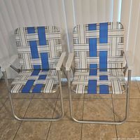 Pair of vintage lawn chairs with nylon webbing in blue and beige geometric stripes on aluminum frames with white plastic armrests.