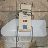 Top-down view of Singer Magic Press 4 electric iron press showing the full base pressing surface and control panel with rotary dial and power cord coiled on top