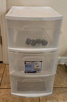 Front view of the 3 drawer white plastic Sterilite cart showing clear drawers and the package of wheels inside the top drawer.