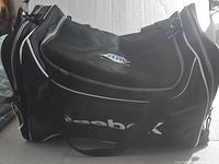 Full view of black Reebok duffle bag with white piping straps.