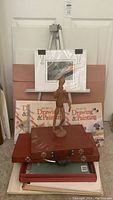 Full view of the art supplies collection with easel, wooden mannequin, art boards, book volumes, and supply cases.