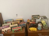 Photo showing multiple Avon boxes featuring vintage car models and collectibles along with loose figurines and decorative pieces on two wooden surfaces.