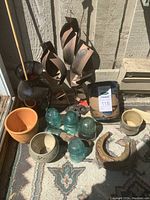 Photo showing metal sculptures, glass insulators, ceramic and clay pots, and horseshoes arranged on a rug.