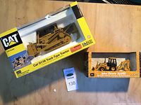 Photo showing both boxed items: Cat D11R Track-Type Tractor and John Deere 310SE Backhoe Loader scale models on a wooden surface.